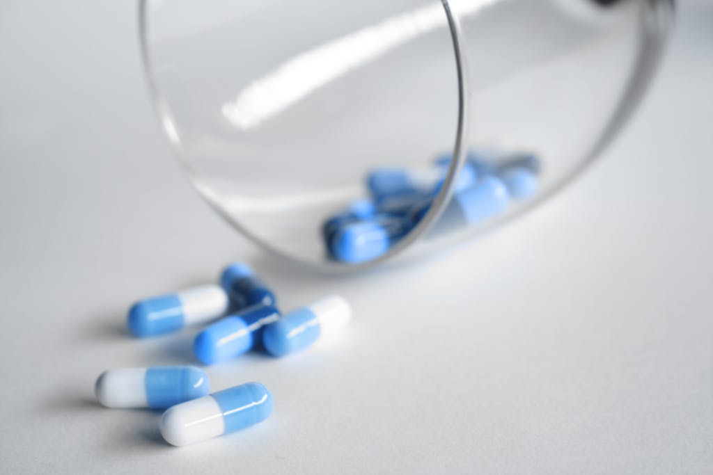 A close-up of blue and white capsules spilling from a glass on a light background.